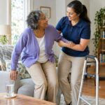 Caregiver supports older woman standing beside a walker at home